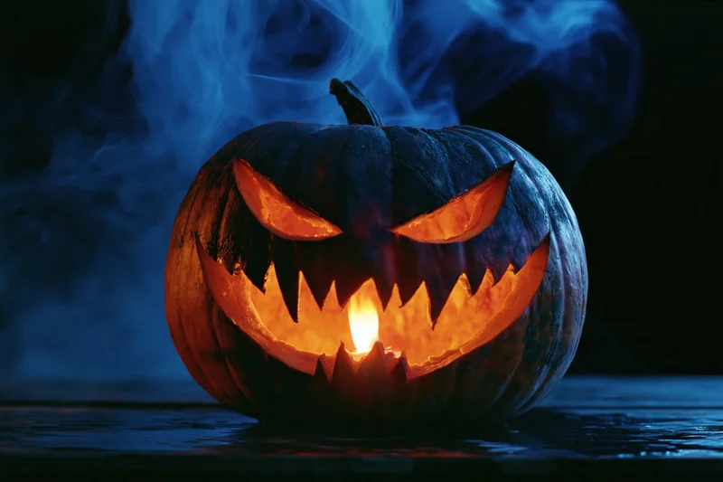 Carved pumpkin with glowing face and blue smoke on dark surface