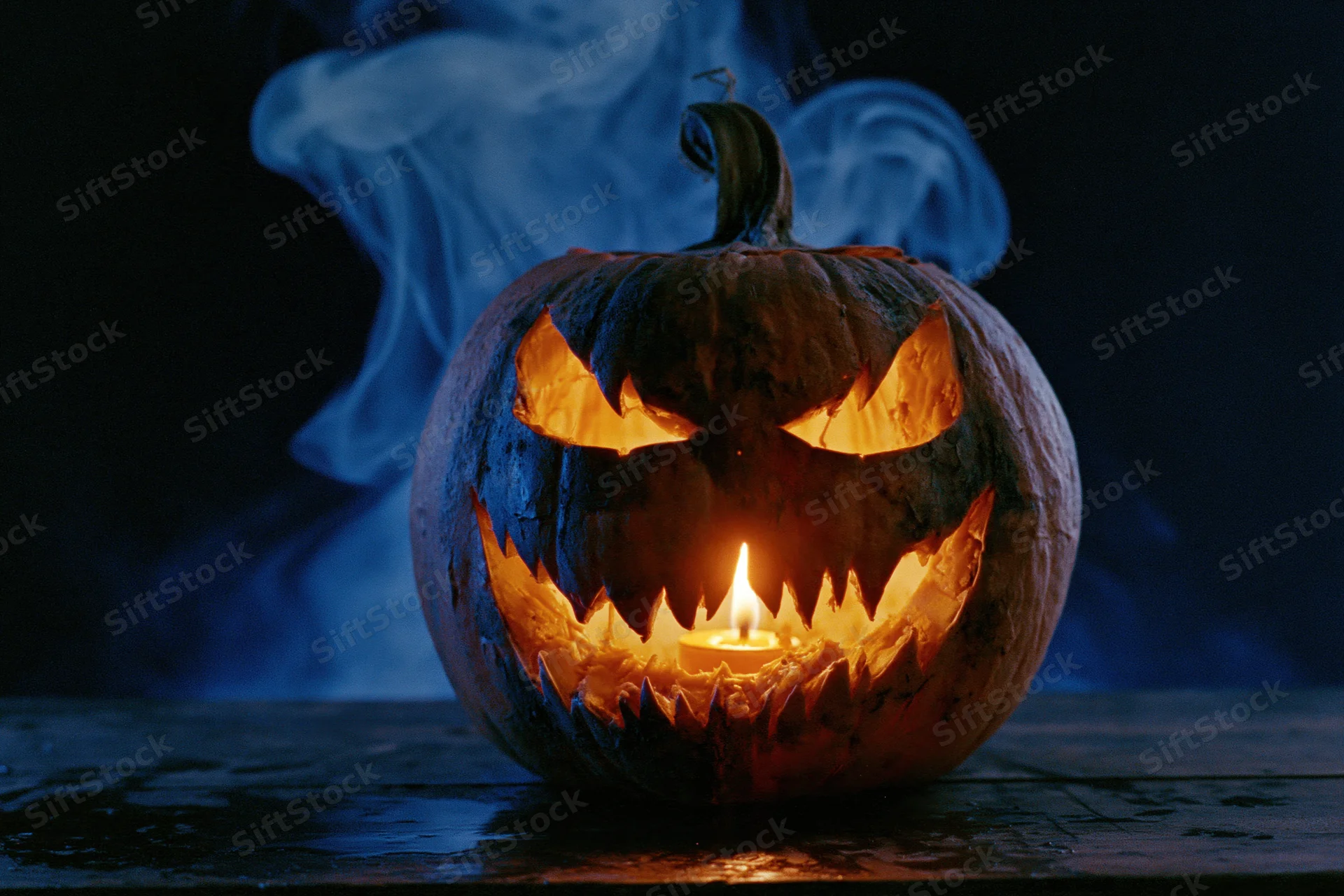Carved pumpkin with glowing candle and blue smoke on dark surface