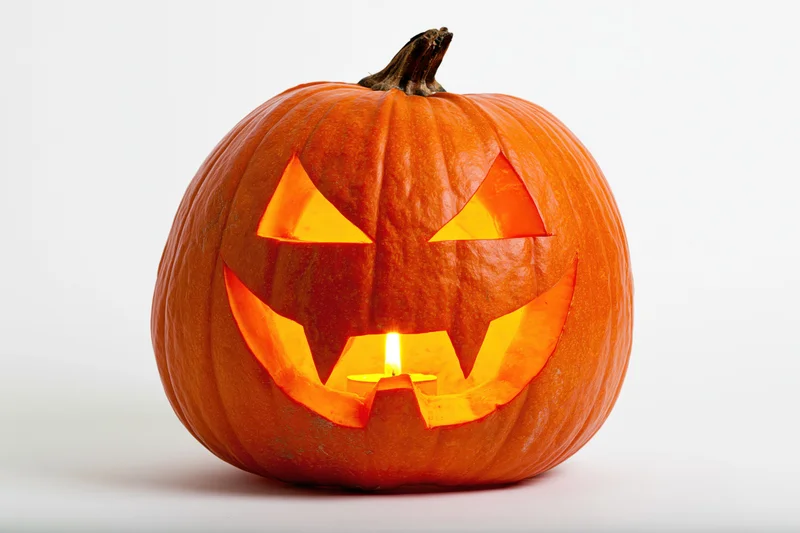Carved pumpkin with glowing candle inside on white background