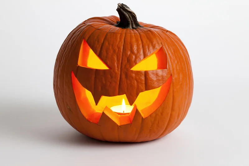 Carved pumpkin with glowing face lit by candle on white background