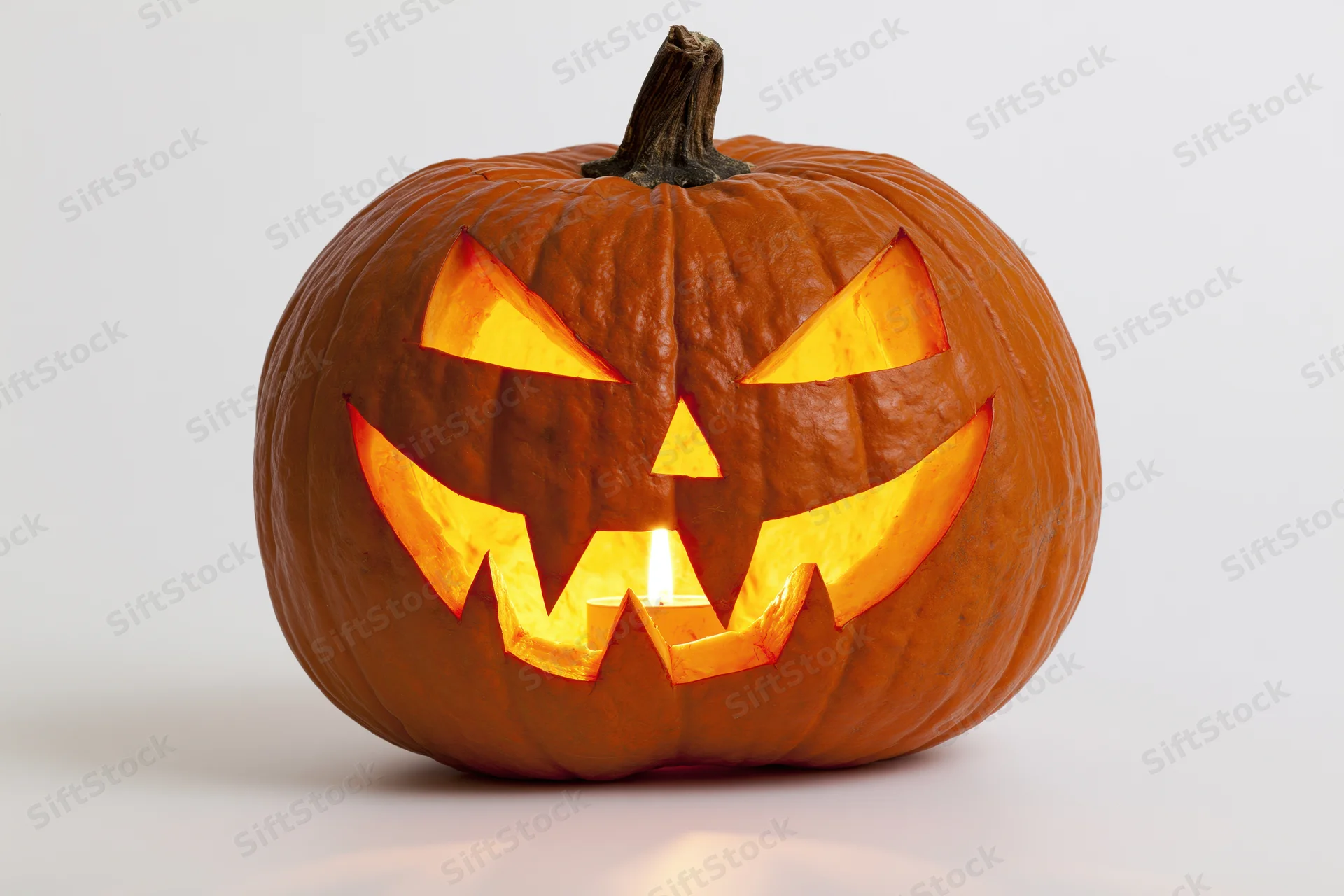 Carved pumpkin with glowing face lit from within on white background