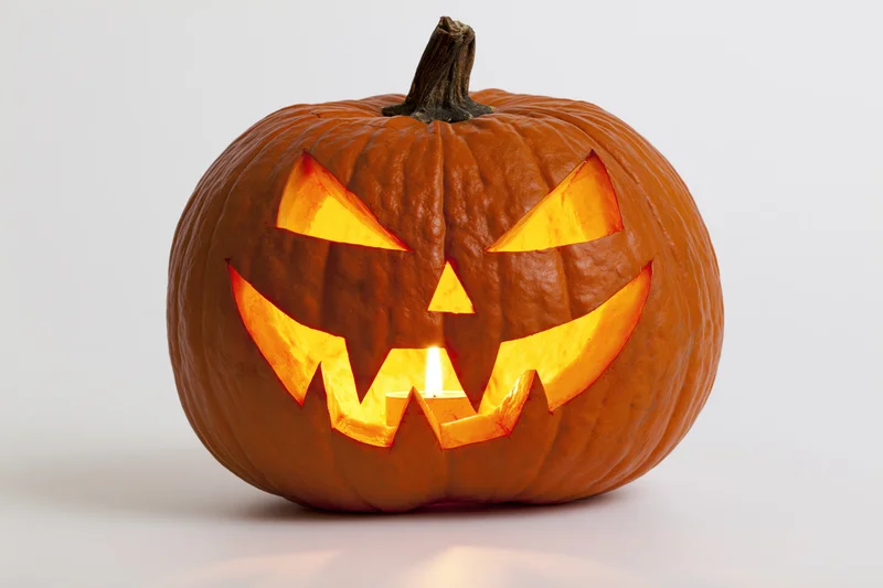 Carved pumpkin with glowing face lit from within on white background
