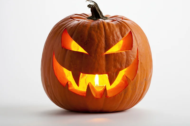 Carved pumpkin with glowing face lit from within on white background