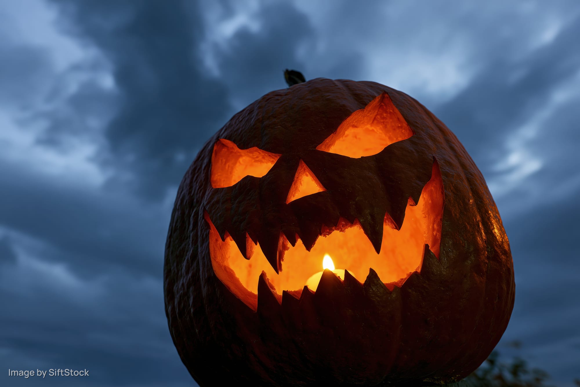Carved pumpkin glowing with candlelight against dark cloudy sky at dusk