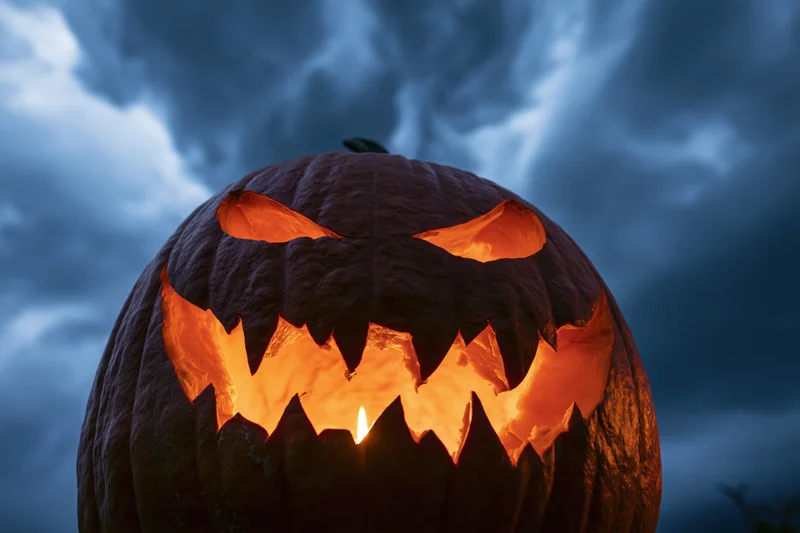 Carved jack-o-lantern glowing with candlelight against stormy night sky