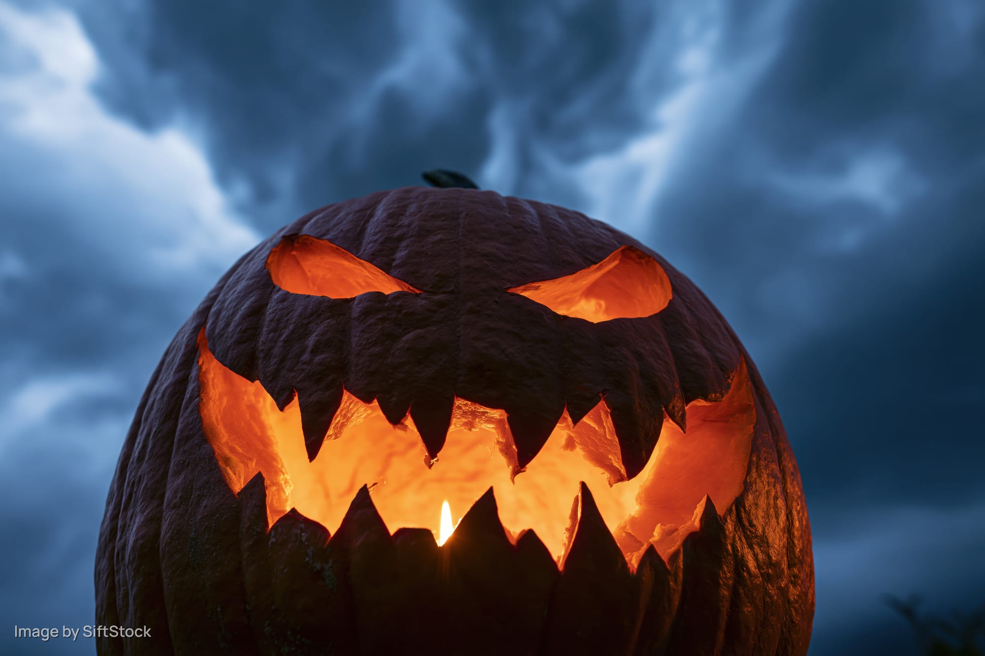 Carved jack-o-lantern glowing with candlelight against stormy night sky
