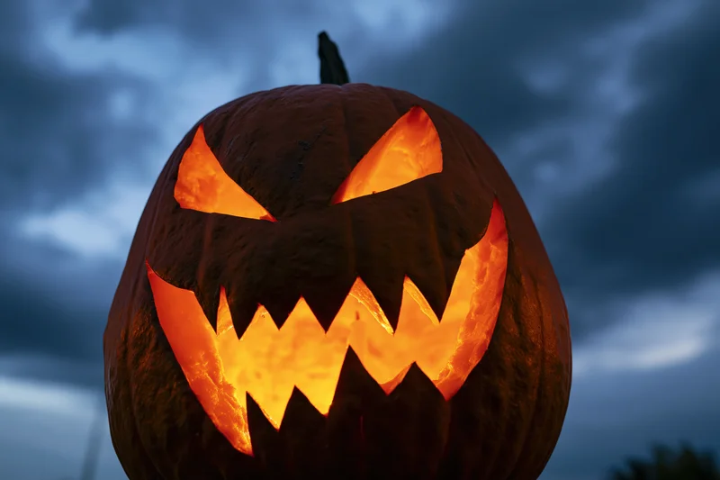 Carved pumpkin with glowing orange face against dark cloudy sky at night