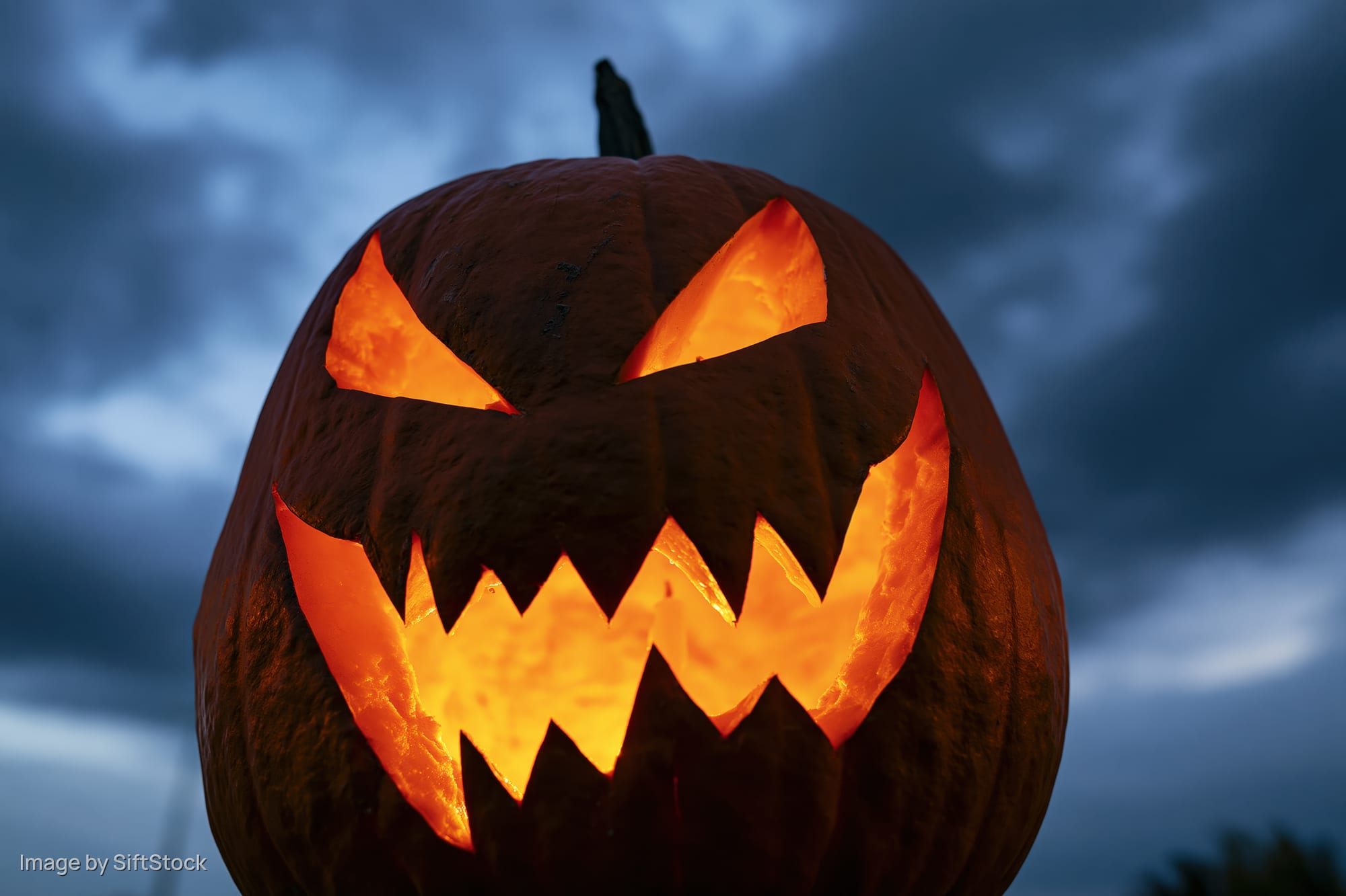 Carved pumpkin with glowing orange face against dark cloudy sky at night