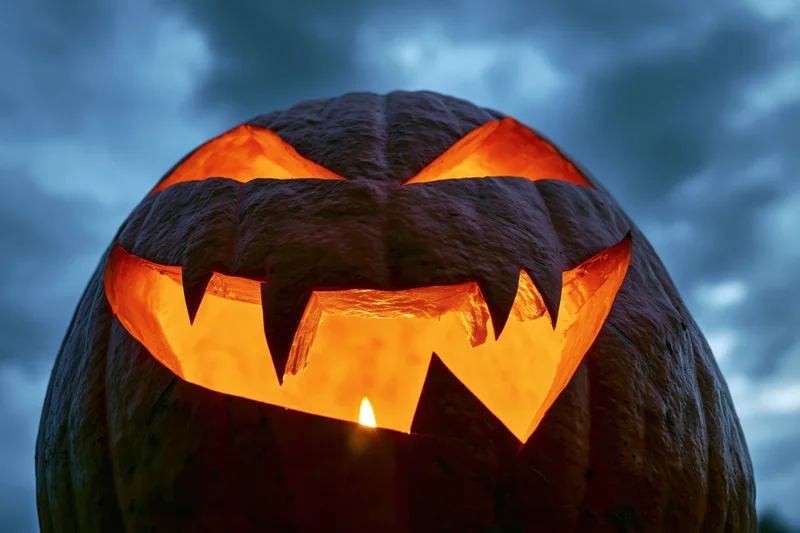 Carved pumpkin glowing with candlelight against dark cloudy sky at night