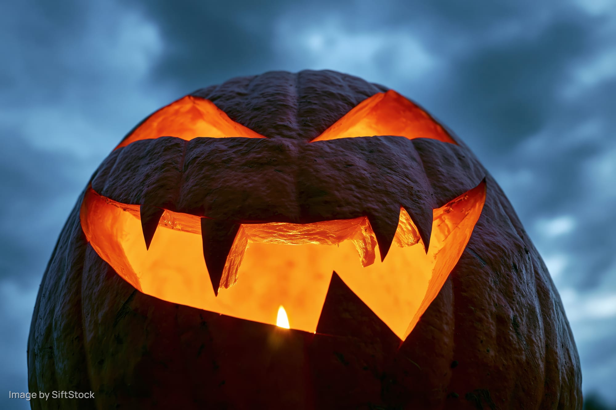 Carved pumpkin glowing with candlelight against dark cloudy sky at night