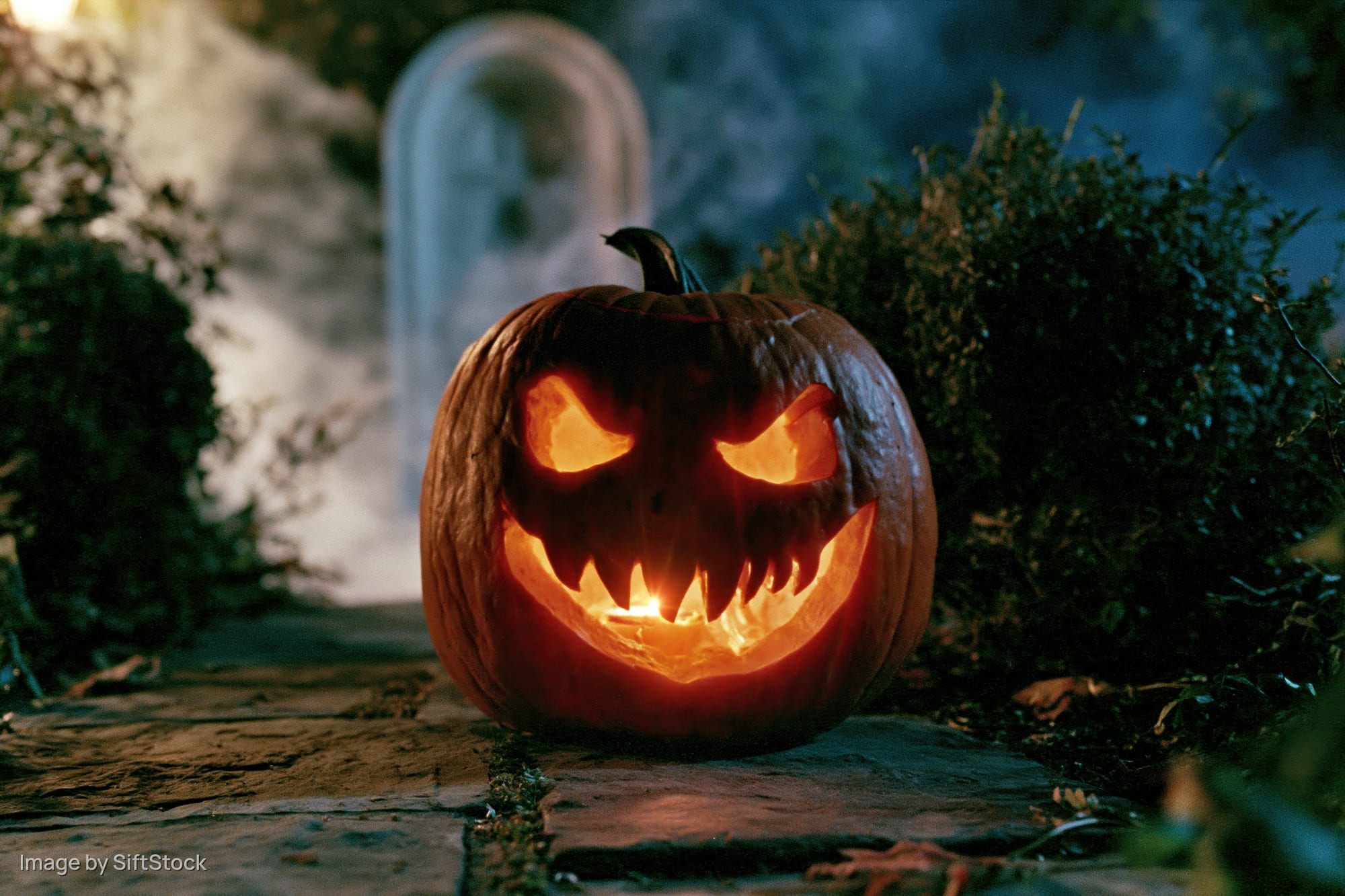 Carved jack-o-lantern with glowing evil grin on stone path in cemetery at night