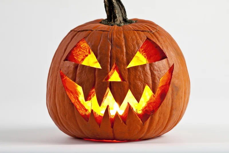 Carved pumpkin with jagged grinning face lit from within on white background
