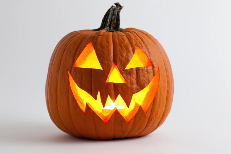 Carved pumpkin with glowing jagged grin on white background
