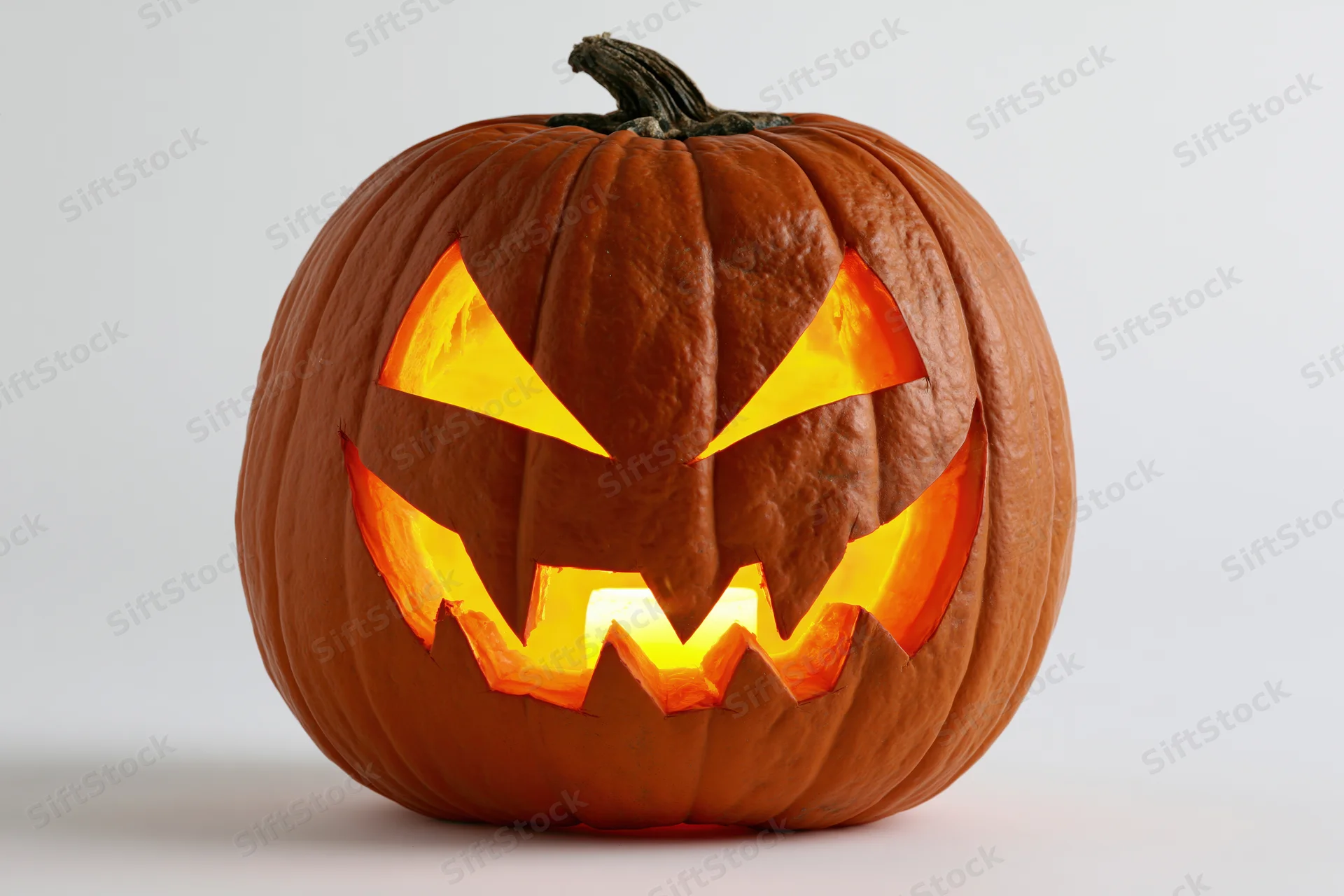 Carved pumpkin with glowing jagged face on white background