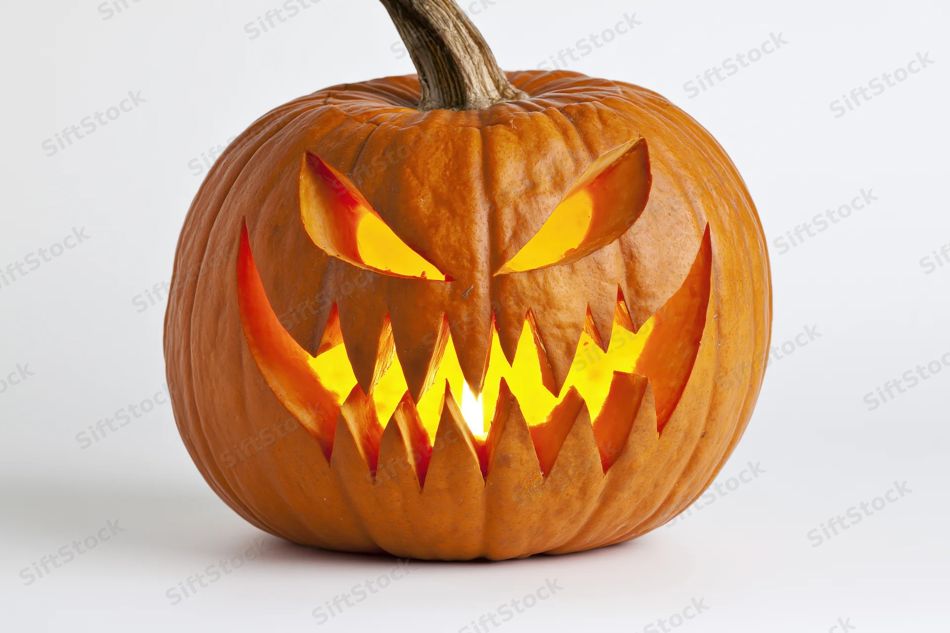 Carved pumpkin with jagged glowing face on white background