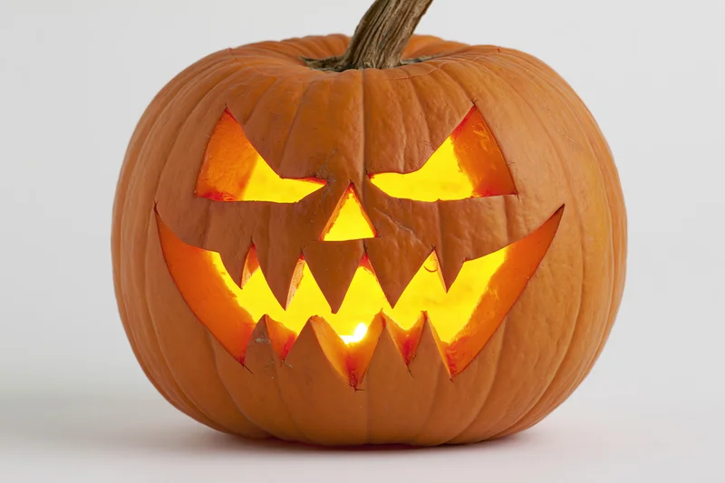Carved pumpkin with jagged face illuminated from within on white background