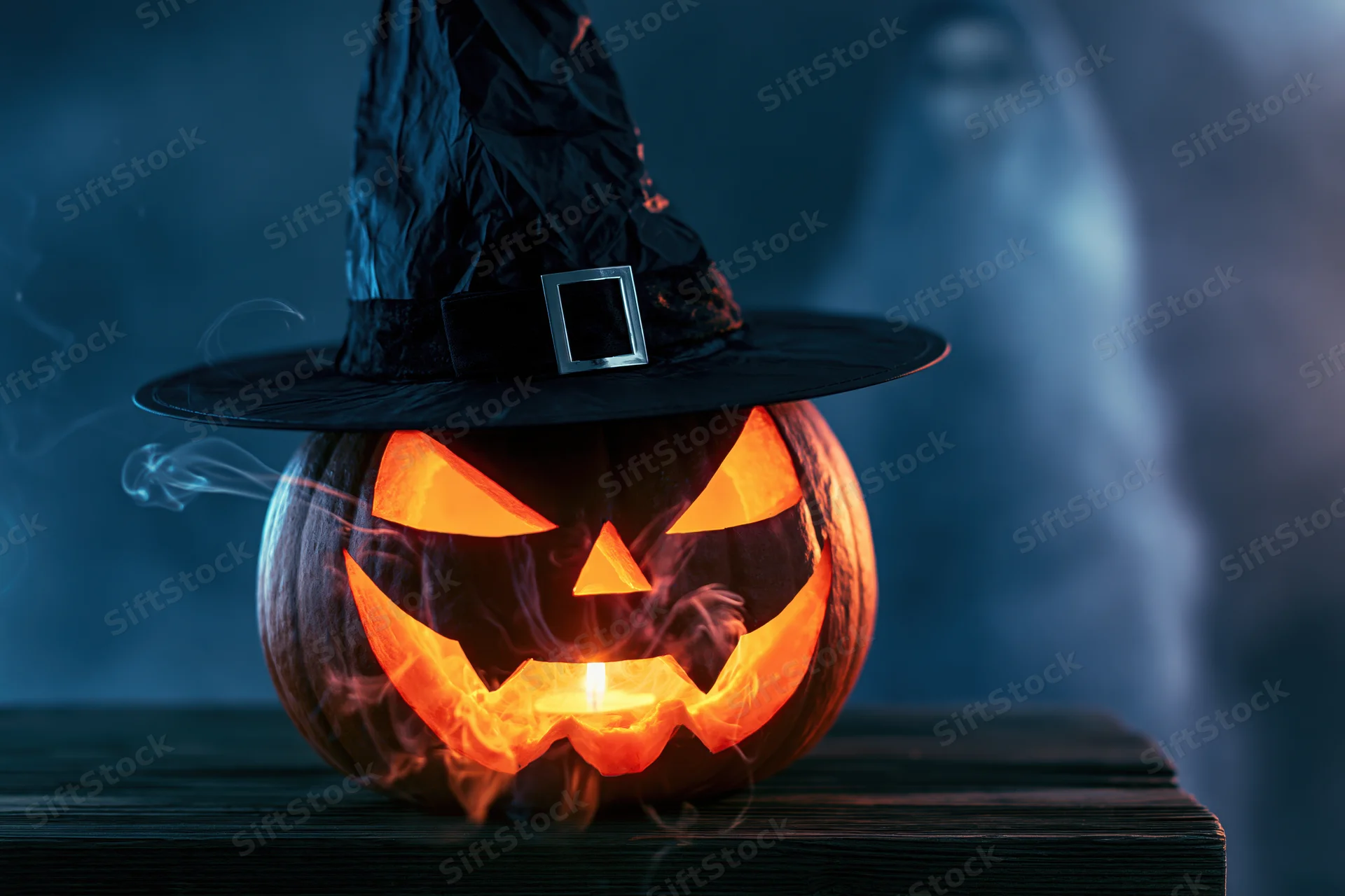 Carved jack-o-lantern with glowing face and witch hat on wooden table at night