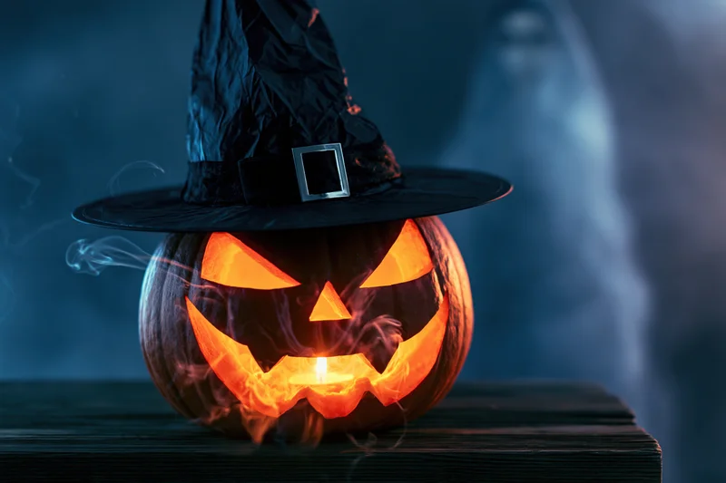 Carved jack-o-lantern with glowing face and witch hat on wooden table at night