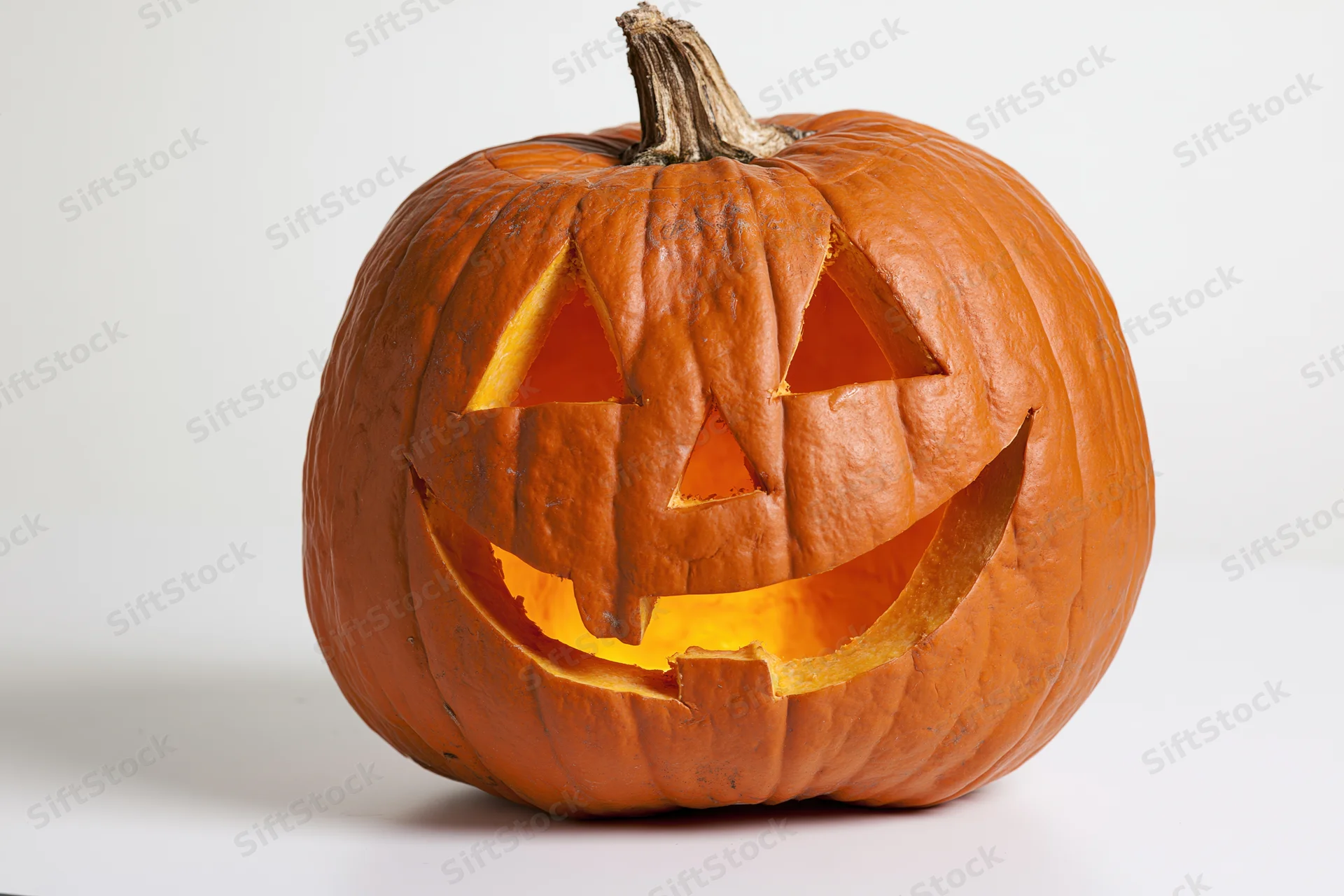 Carved pumpkin with glowing grinning face on white background