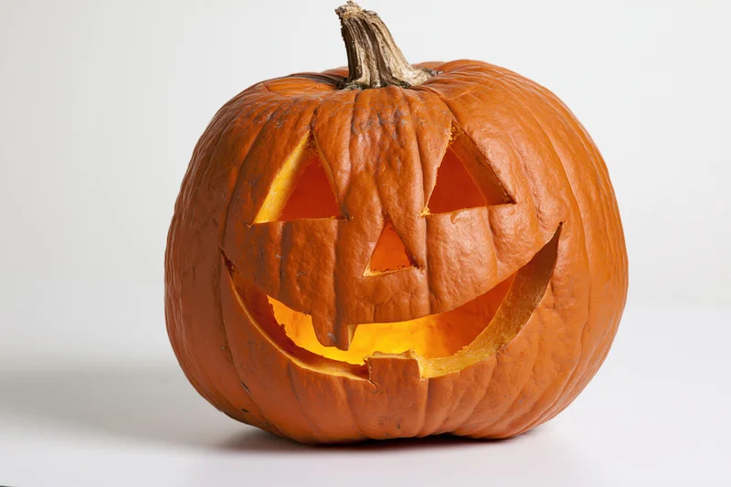 Carved pumpkin with glowing grinning face on white background