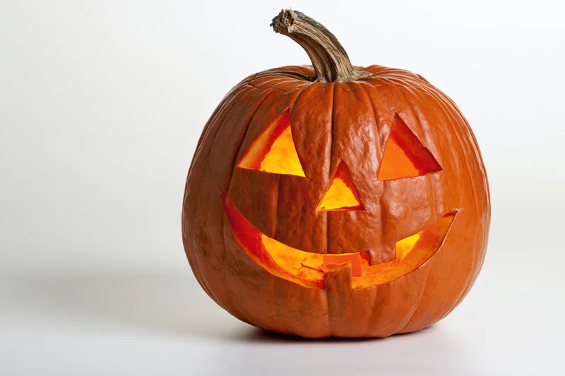 Carved pumpkin with glowing grinning face on white background