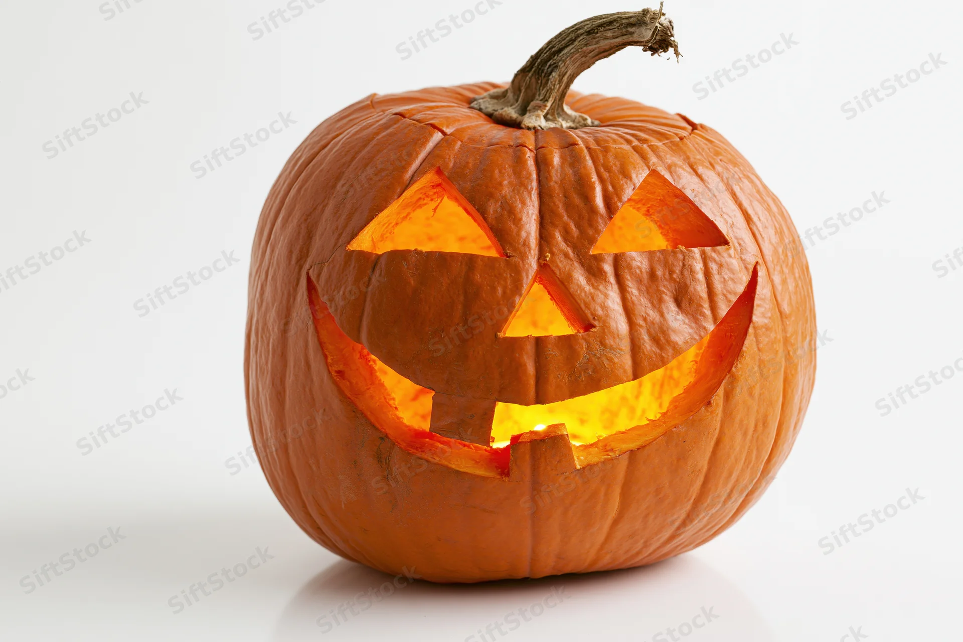 Carved pumpkin with glowing grinning face on white background