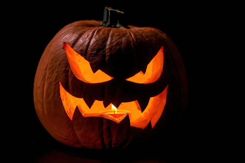 Carved pumpkin with menacing face illuminated by candle in dark setting