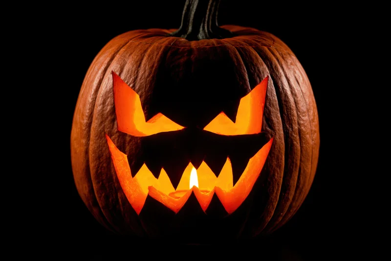 Carved pumpkin with menacing face lit from within against black background