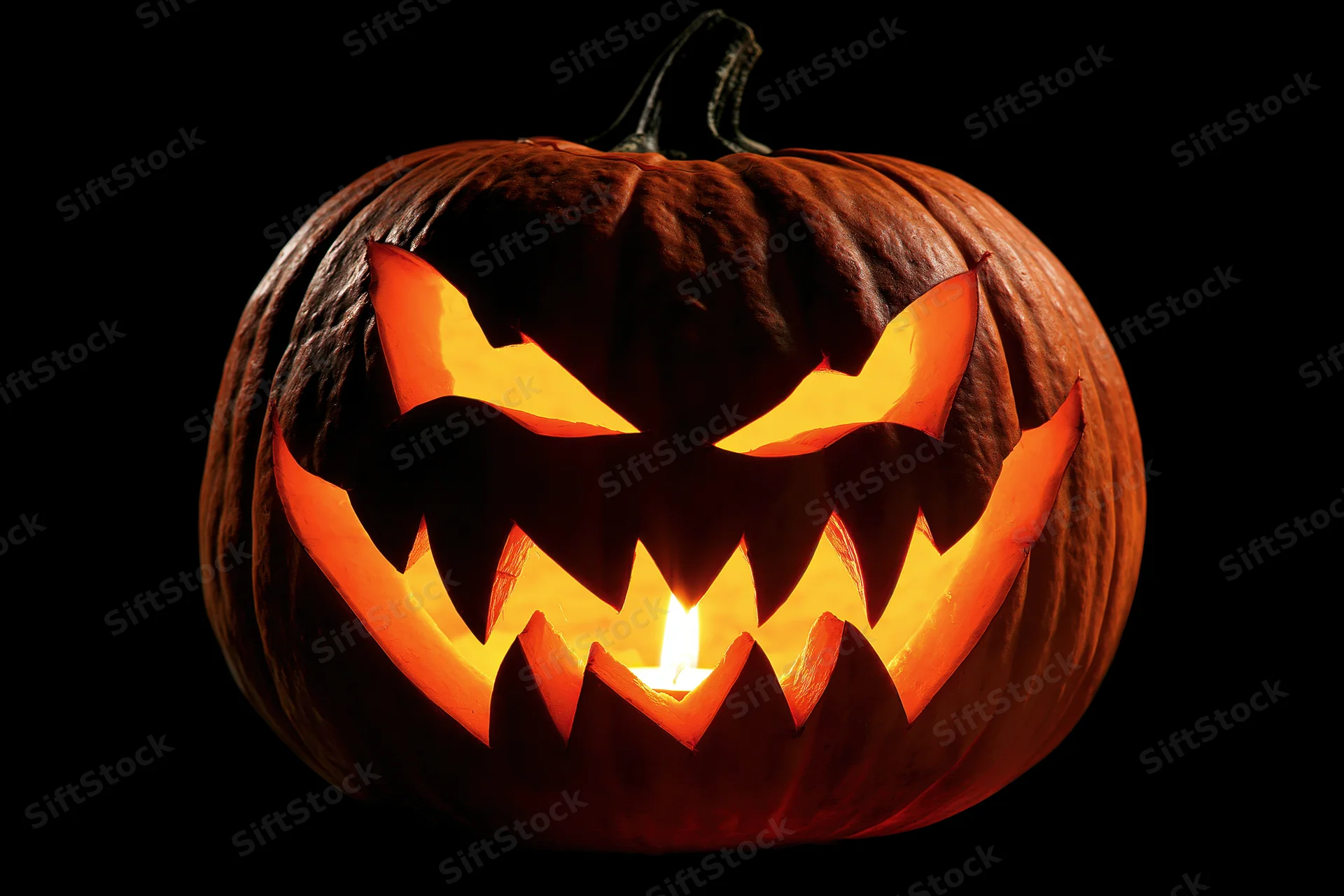 Carved pumpkin with menacing face illuminated by candlelight against black background