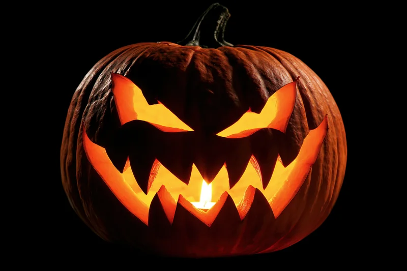 Carved pumpkin with menacing face illuminated by candlelight against black background