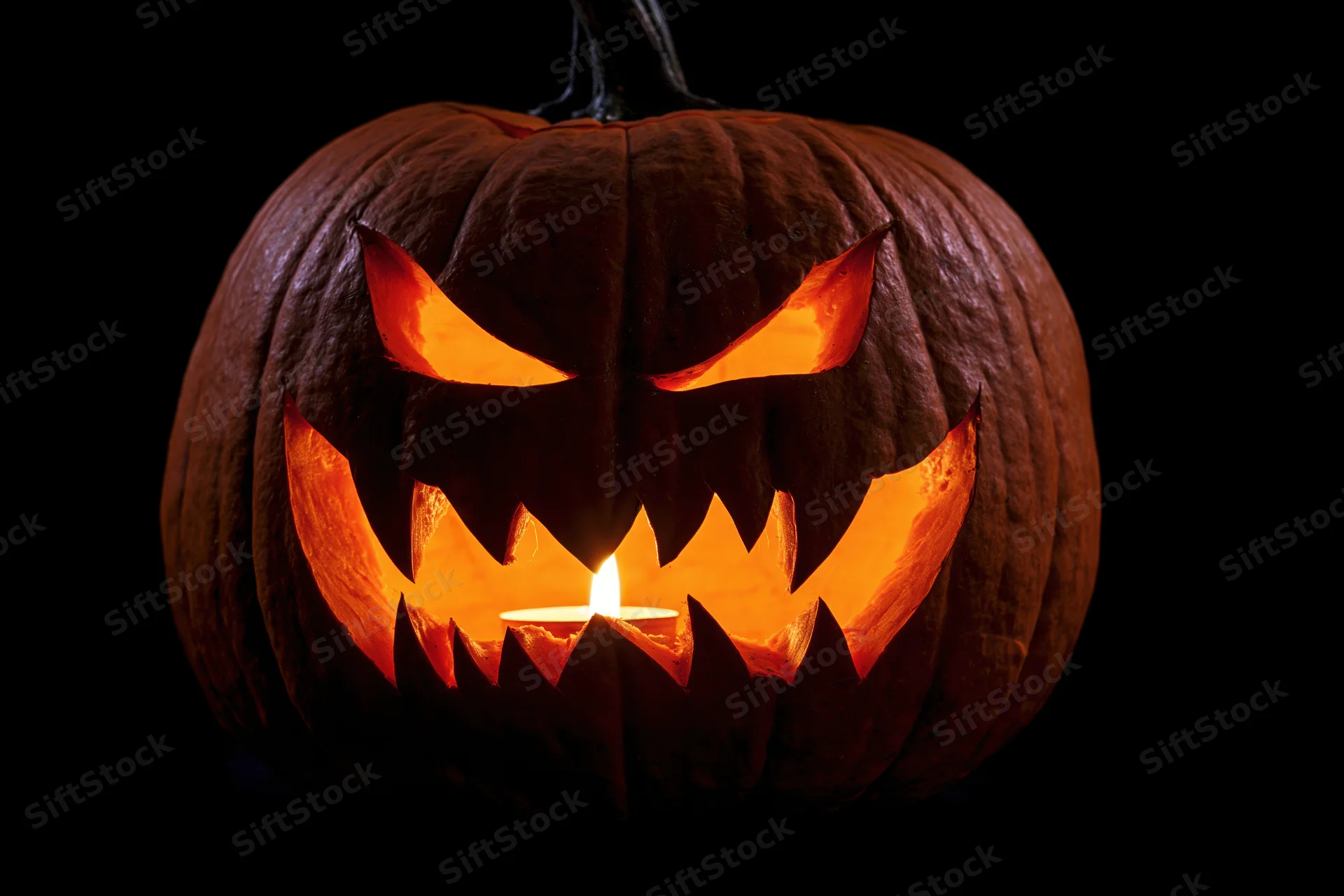 Carved pumpkin with menacing face lit by candle against black background