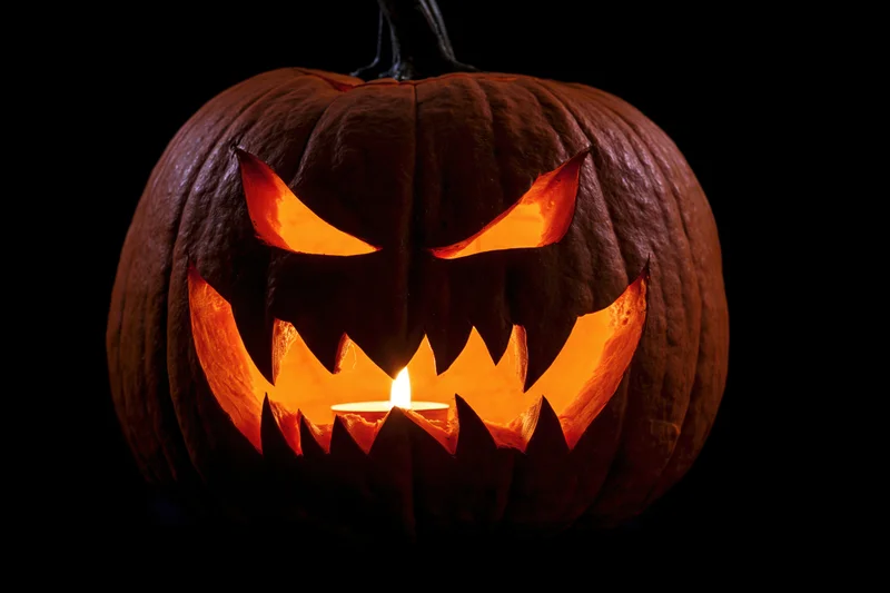 Carved pumpkin with menacing face lit by candle against black background