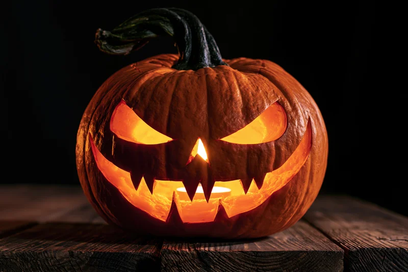 Carved pumpkin with menacing face glowing from within on wooden surface
