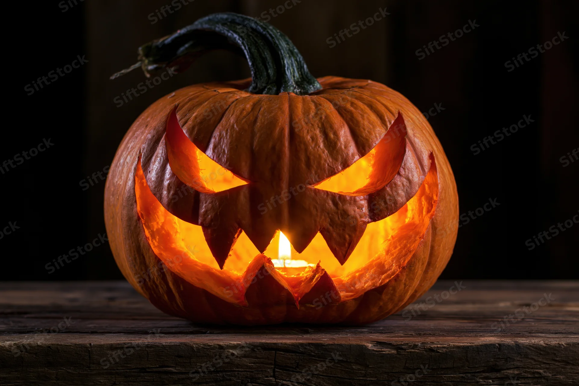 Carved pumpkin with menacing face glowing from candlelight on wooden table