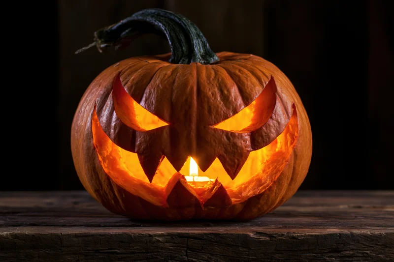 Carved pumpkin with menacing face glowing from candlelight on wooden table