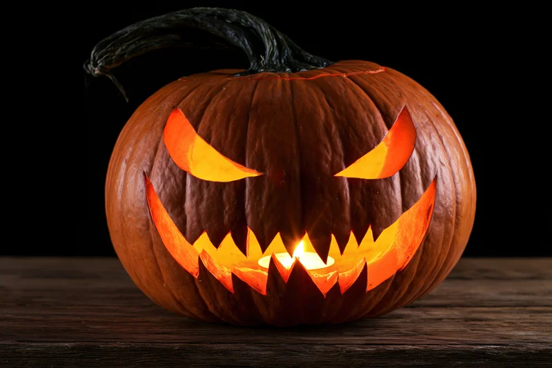 Carved pumpkin with glowing menacing face on wooden table
