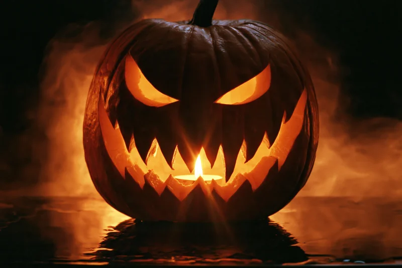 Carved jack-o-lantern with jagged grin glowing in dark water surrounded by smoke