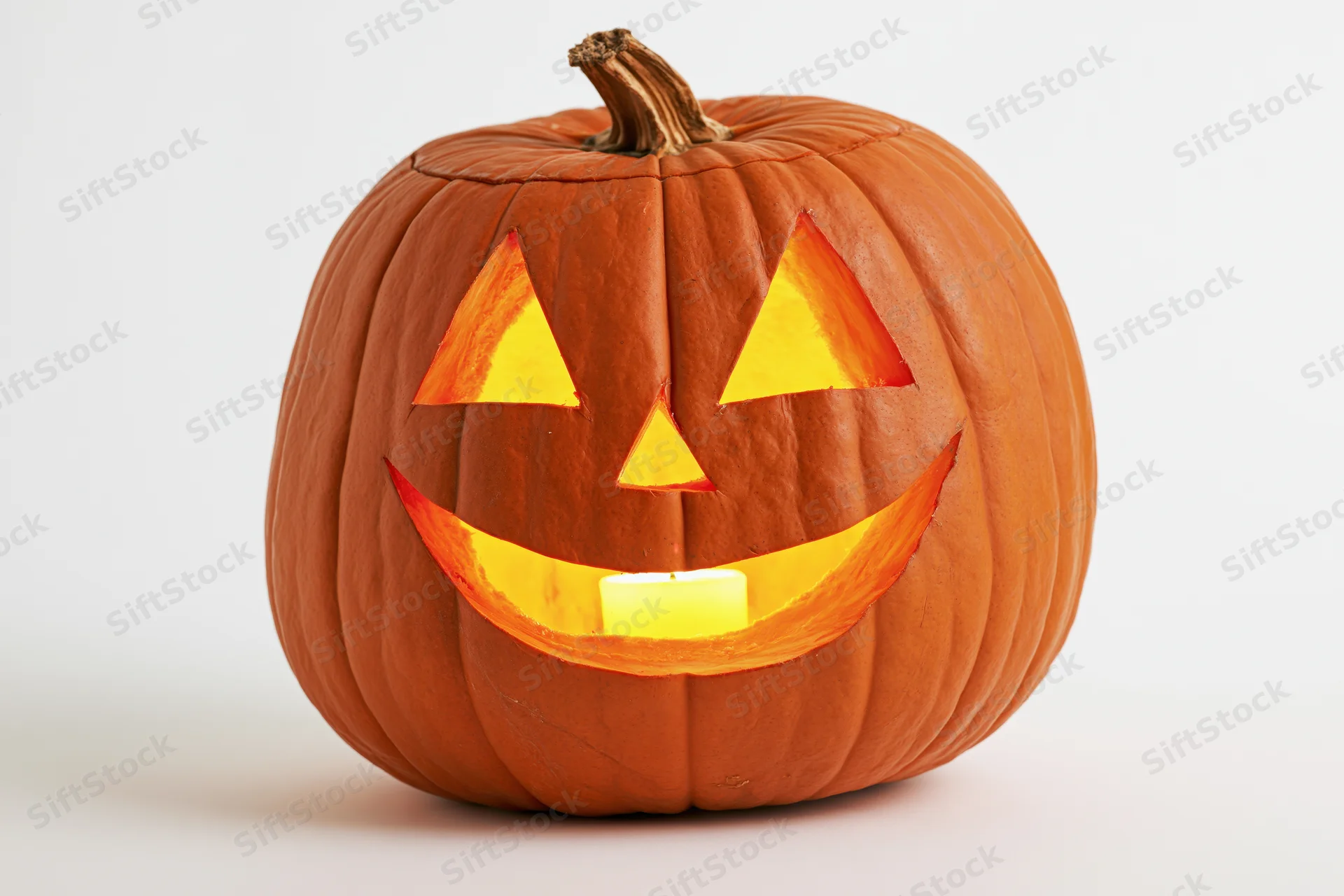 Carved pumpkin with smiling triangular eyes and glowing candle inside, isolated on white background
