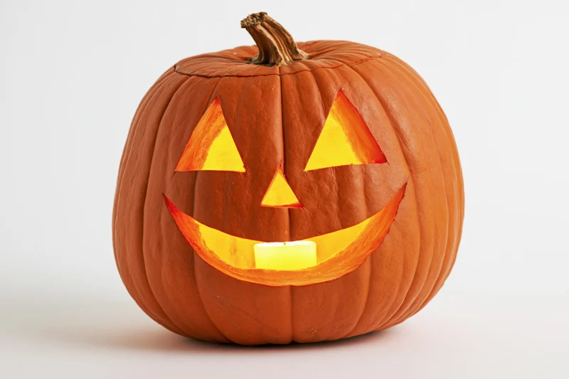 Carved pumpkin with smiling triangular eyes and glowing candle inside, isolated on white background