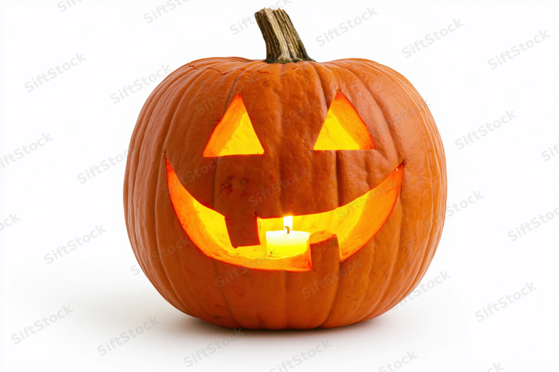 Carved pumpkin with triangular eyes and smiling mouth lit by candle on white background