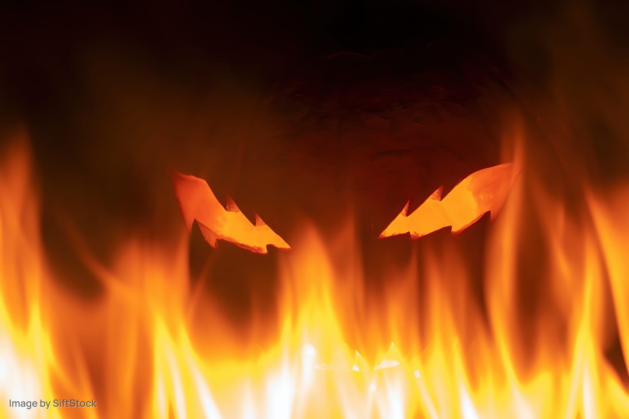 Carved jack-o-lantern with jagged glowing eyes surrounded by flames at night