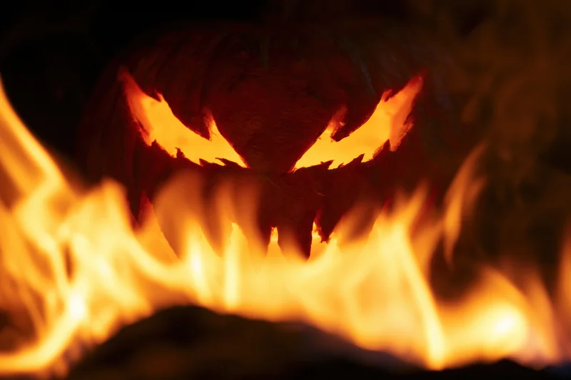 Carved jack-o-lantern with jagged eyes glowing behind flames at night