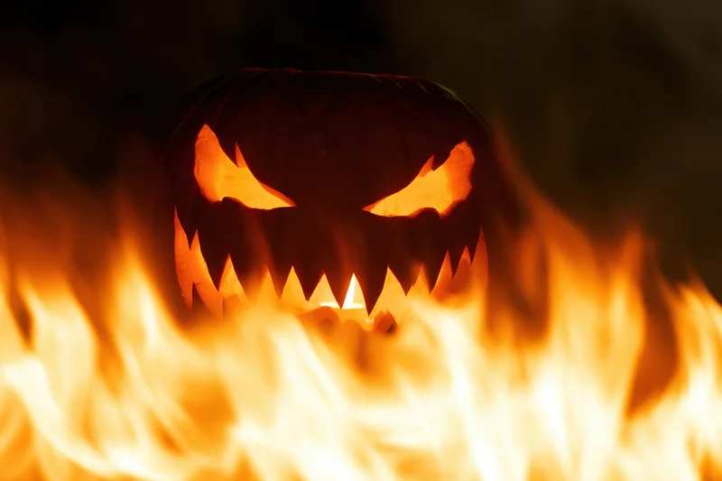 Carved jack-o-lantern glowing with jagged eyes surrounded by flames at night