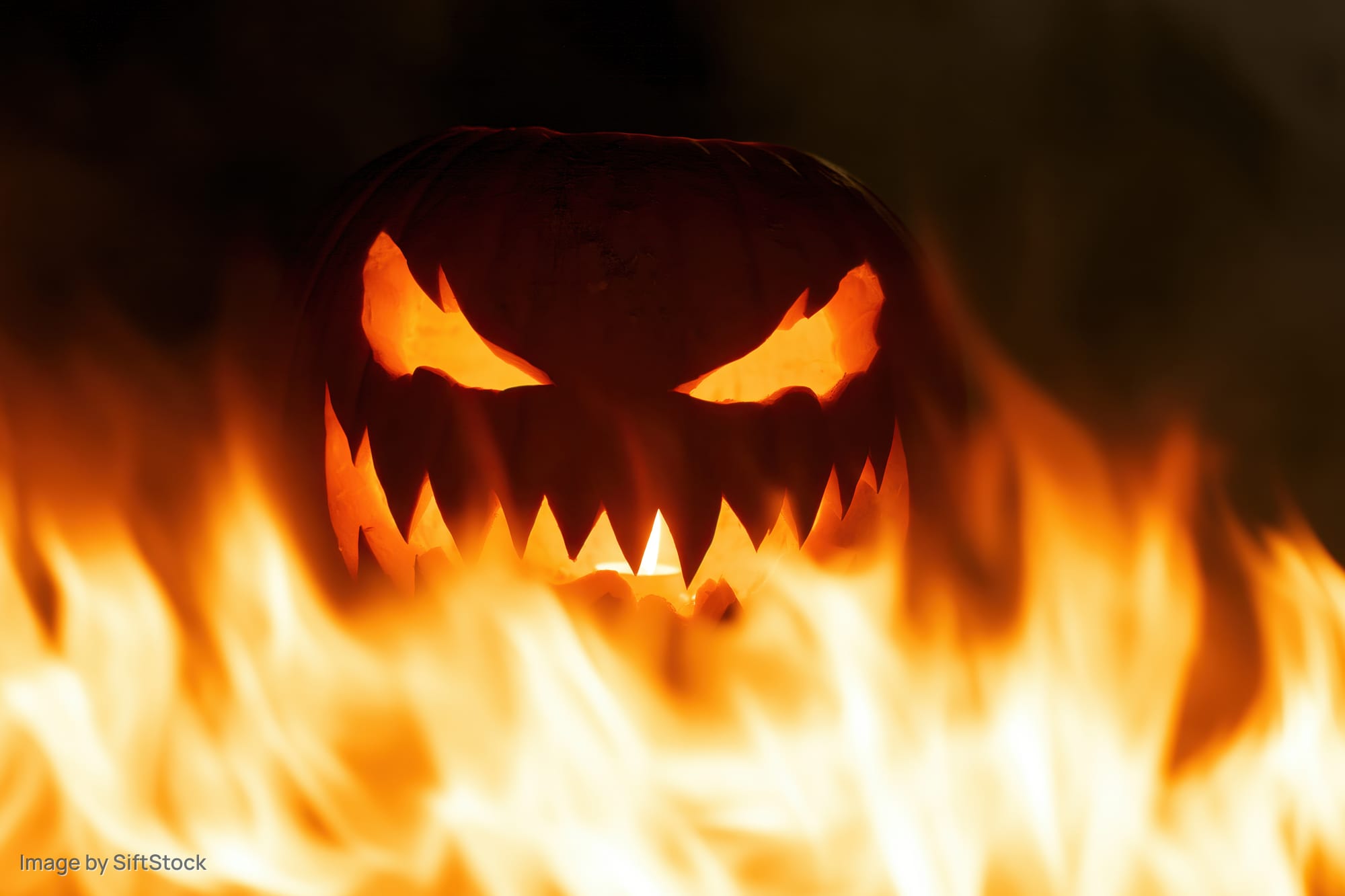 Carved jack-o-lantern glowing with jagged eyes surrounded by flames at night