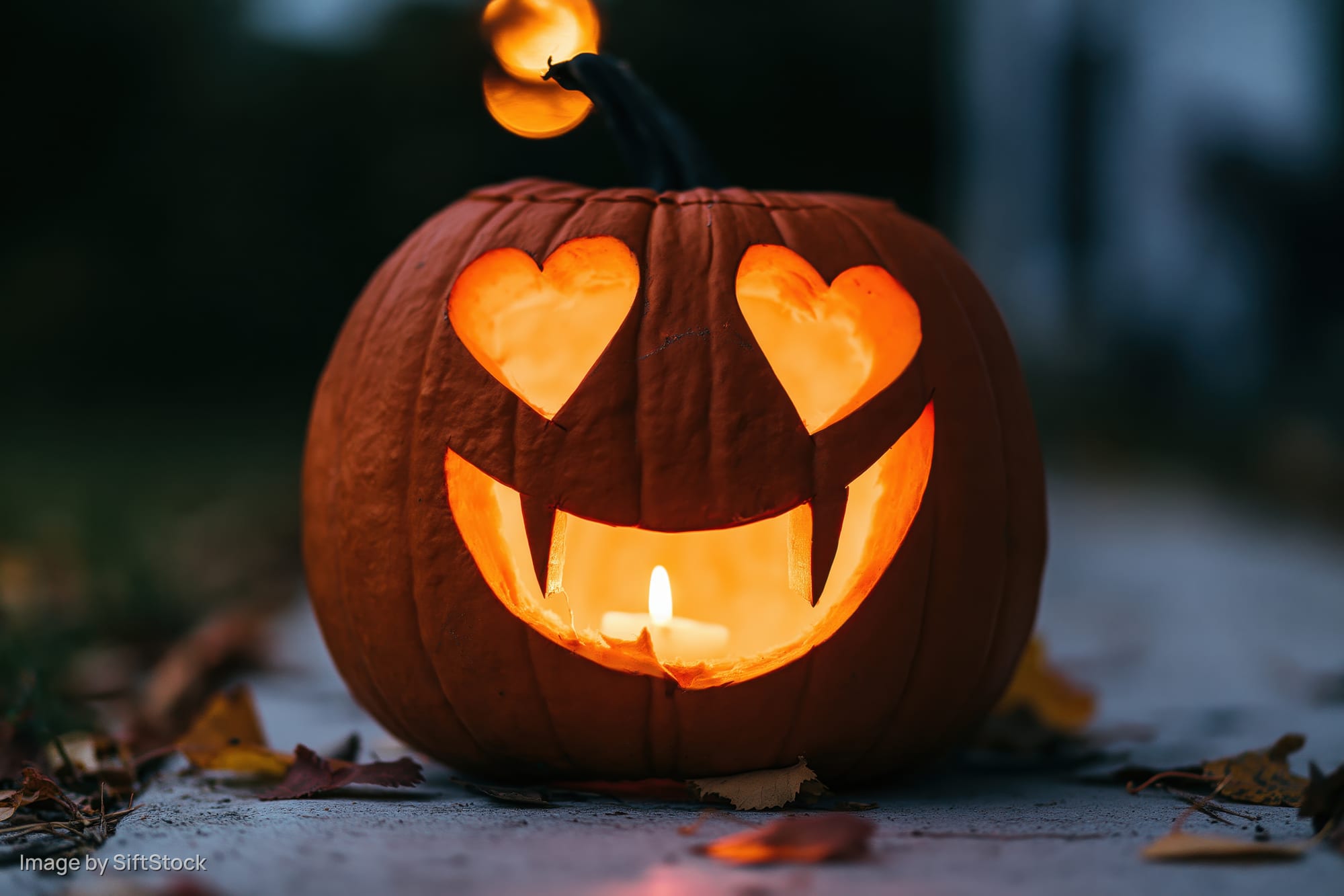 Carved pumpkin with heart-shaped eyes and smiling mouth lit by candle on sidewalk at night