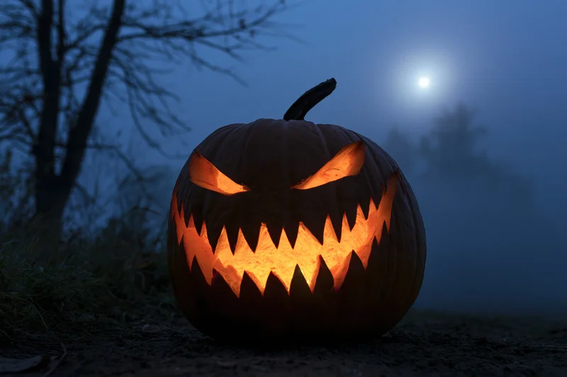 Carved pumpkin with jagged grin glowing in foggy night under moonlight