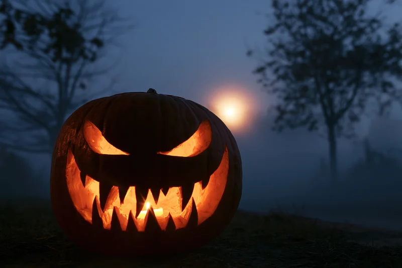 Carved pumpkin with jagged grin glowing in foggy night outdoors