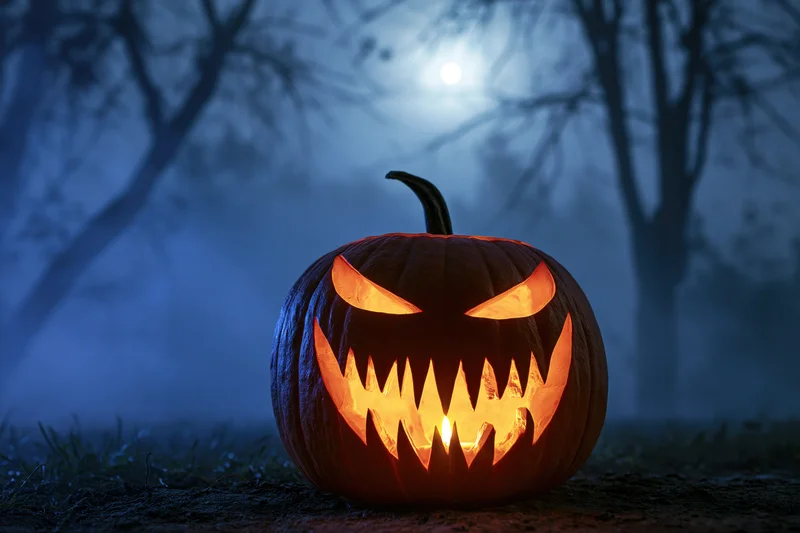 Carved pumpkin with jagged grin glowing in foggy forest at night