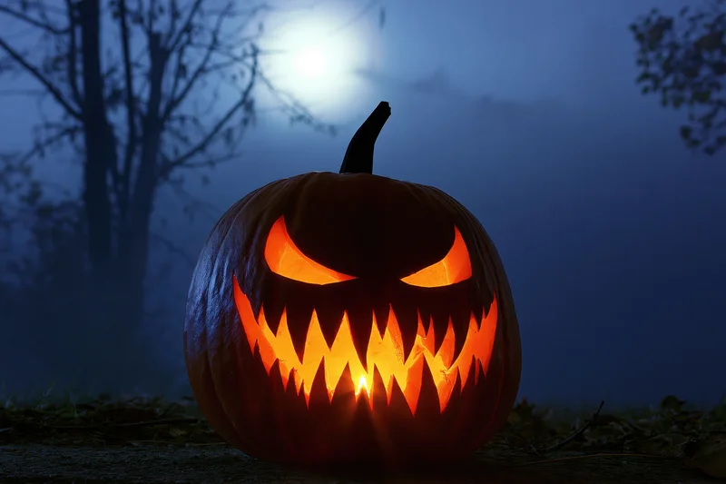 Carved pumpkin with jagged grin glowing in foggy forest at night under moonlight
