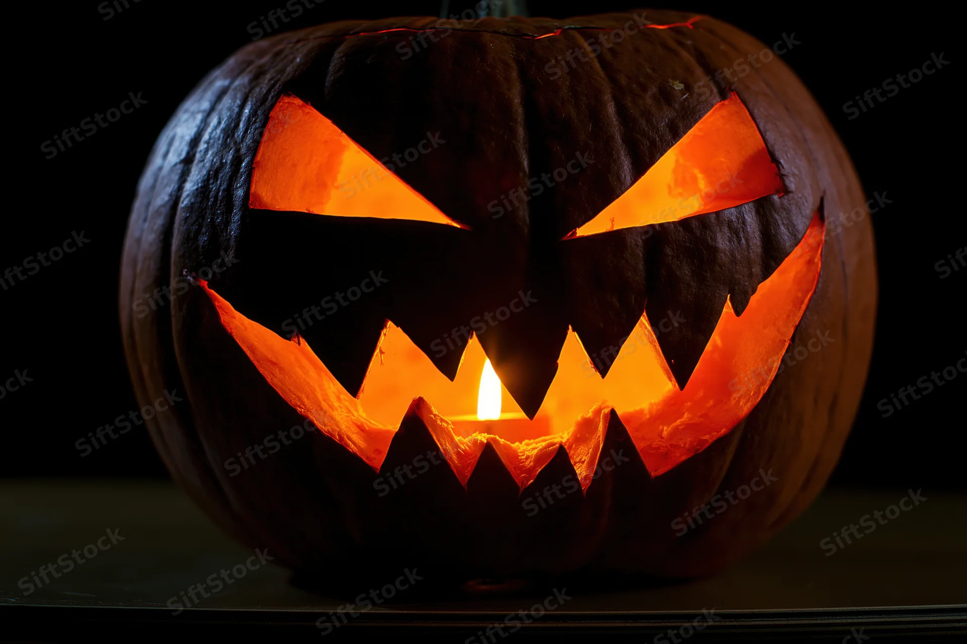 Carved pumpkin with jagged grin lit from within on dark surface